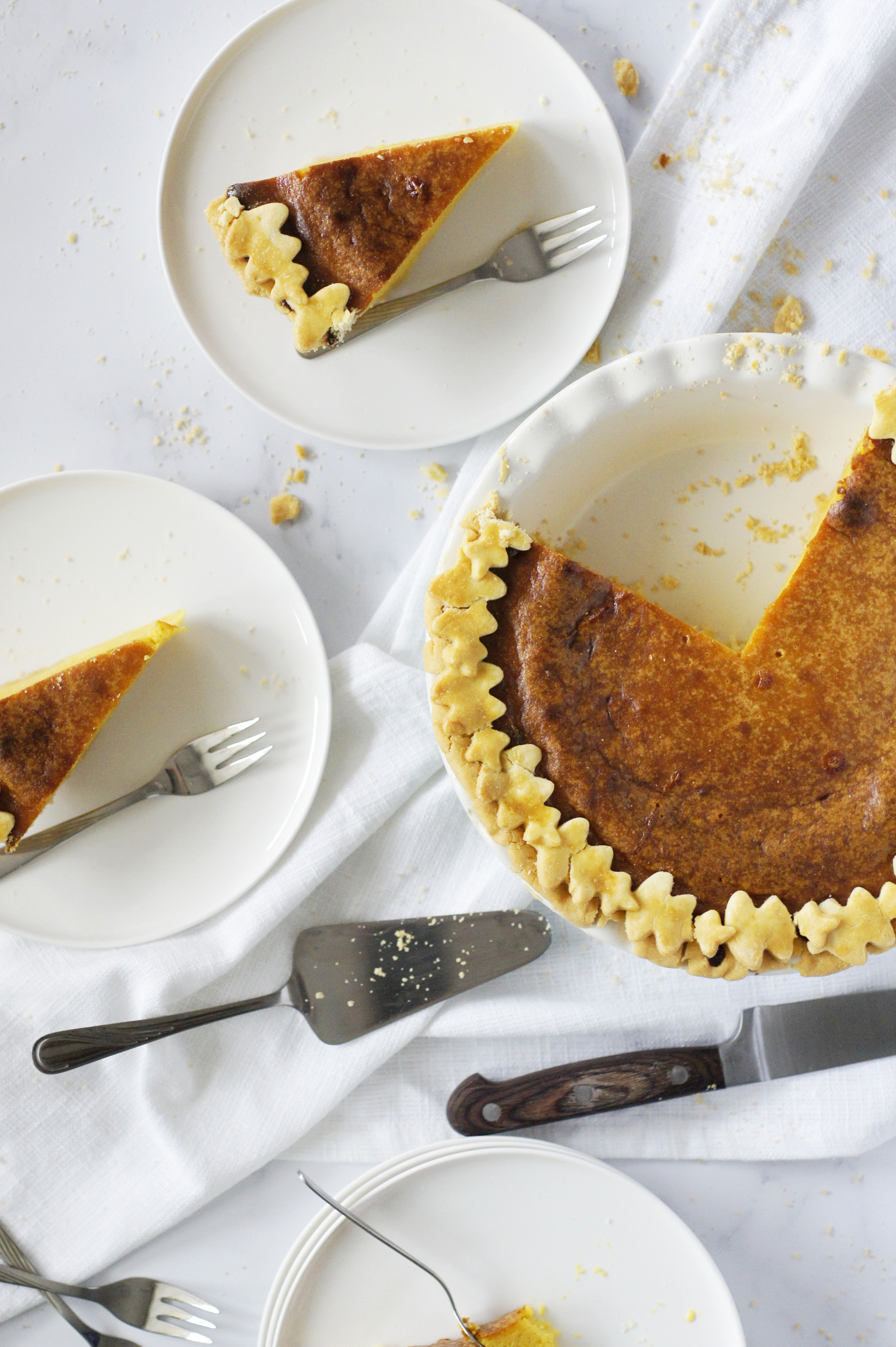 na stole stoi pumpkin pie w formie do pie i kawałki ciasta na białych talerzykach deserowych